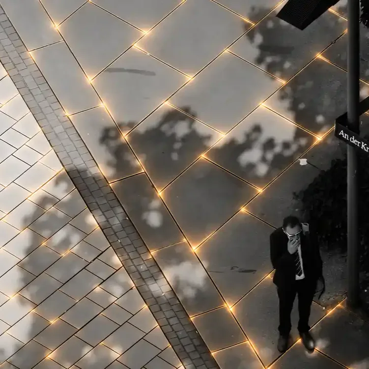 Acera con baldosas solares inteligentes Suntile iluminadas en las juntas y peatón caminando