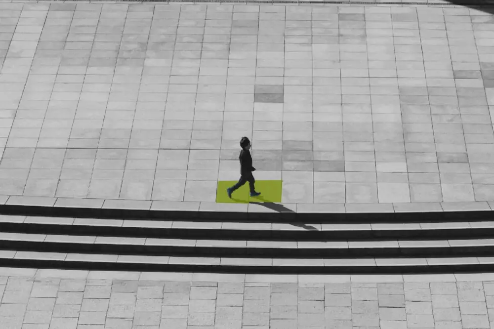 Peatón caminando sobre una baldosa Suntile resaltada en verde en una plaza peatonal: pavimento de terrazo solar e inteligente de Deca Technologies